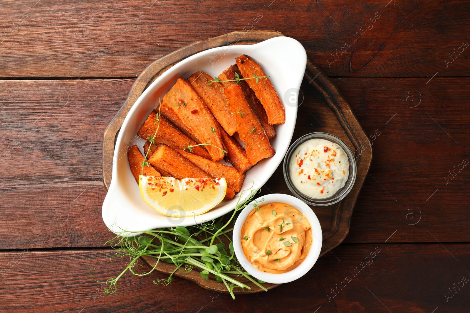 Photo of Pieces of tasty cooked sweet potato in baking dish served on wooden table, top view