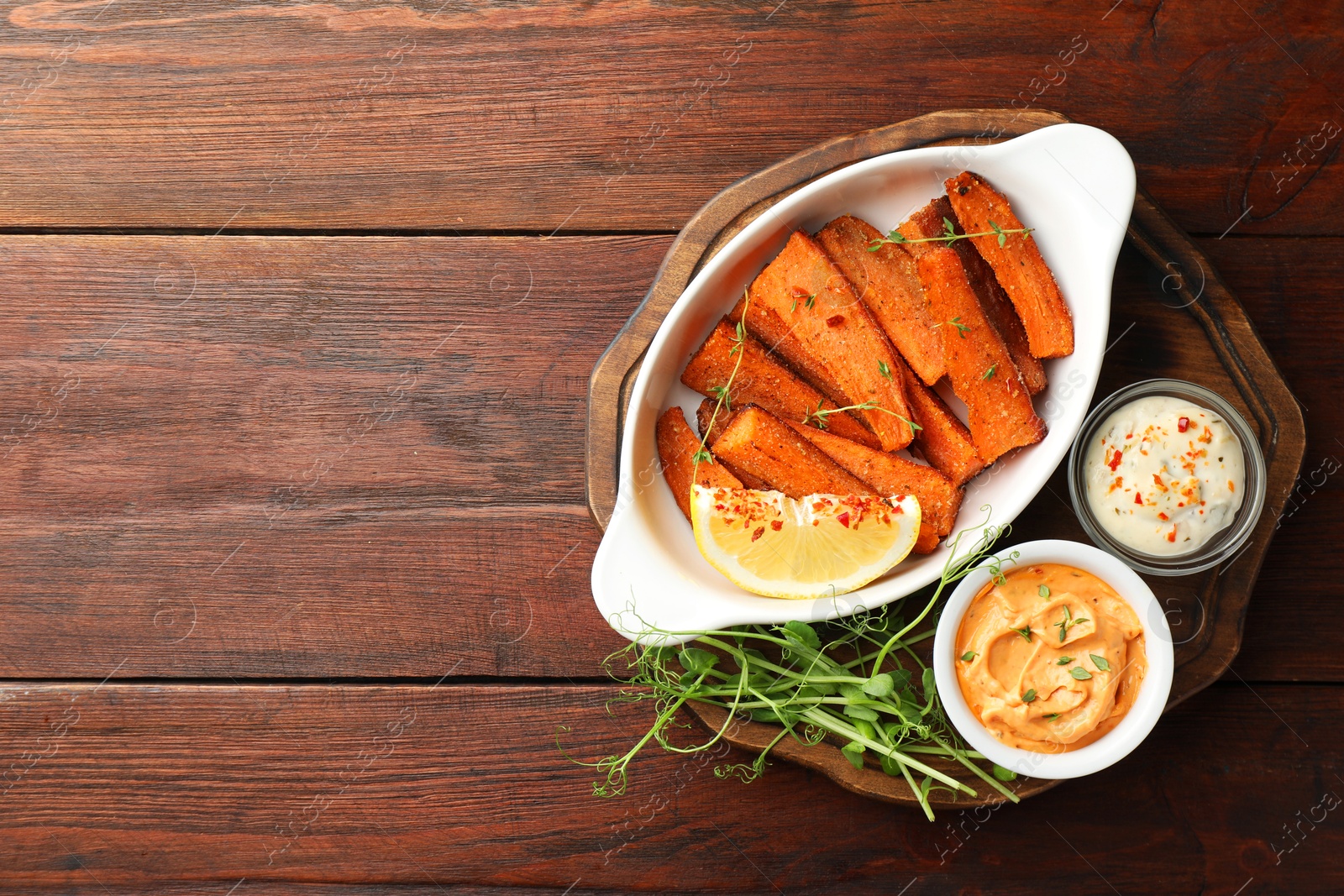 Photo of Pieces of tasty cooked sweet potato in baking dish served on wooden table, top view. Space for text