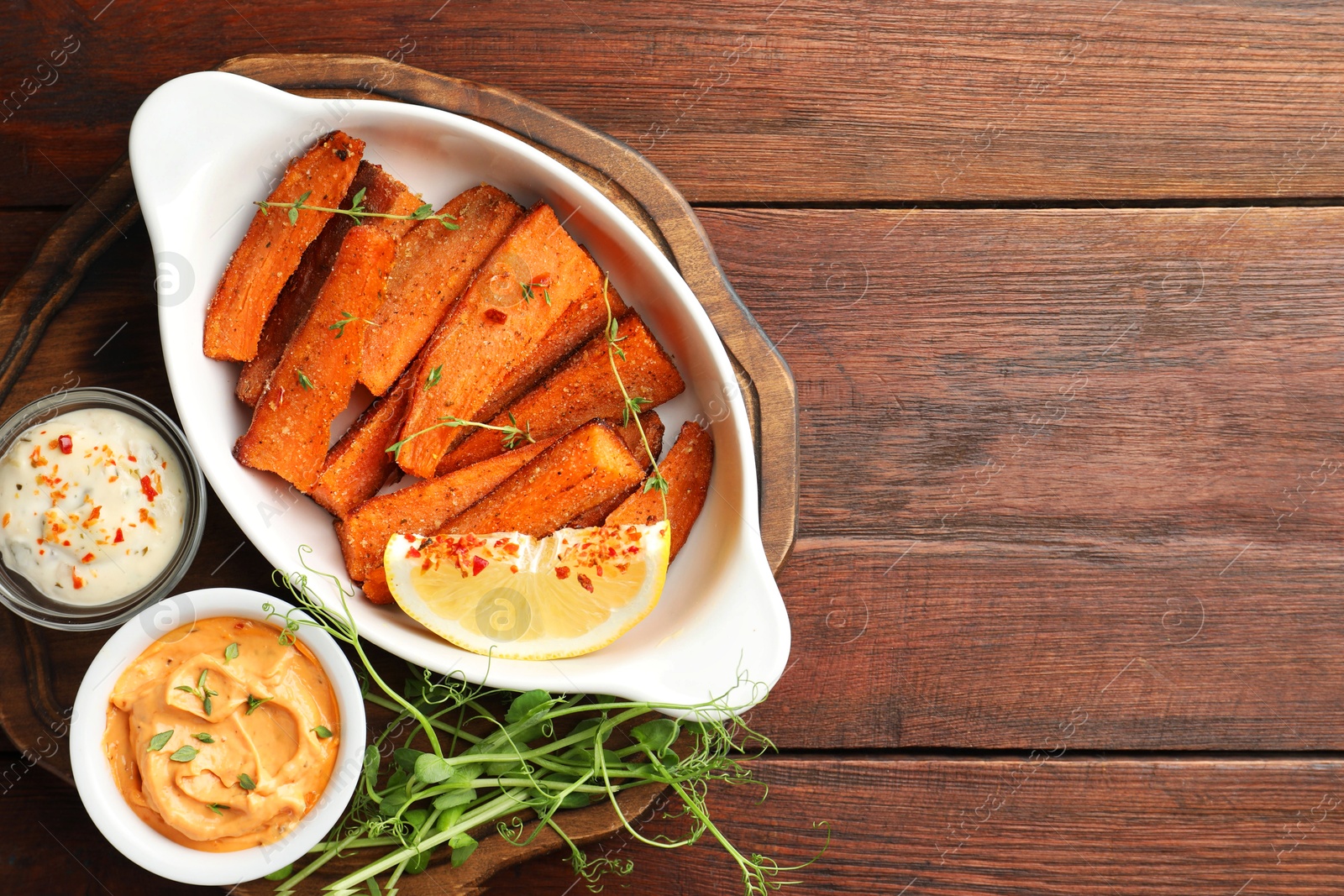 Photo of Pieces of tasty cooked sweet potato in baking dish served on wooden table, top view. Space for text