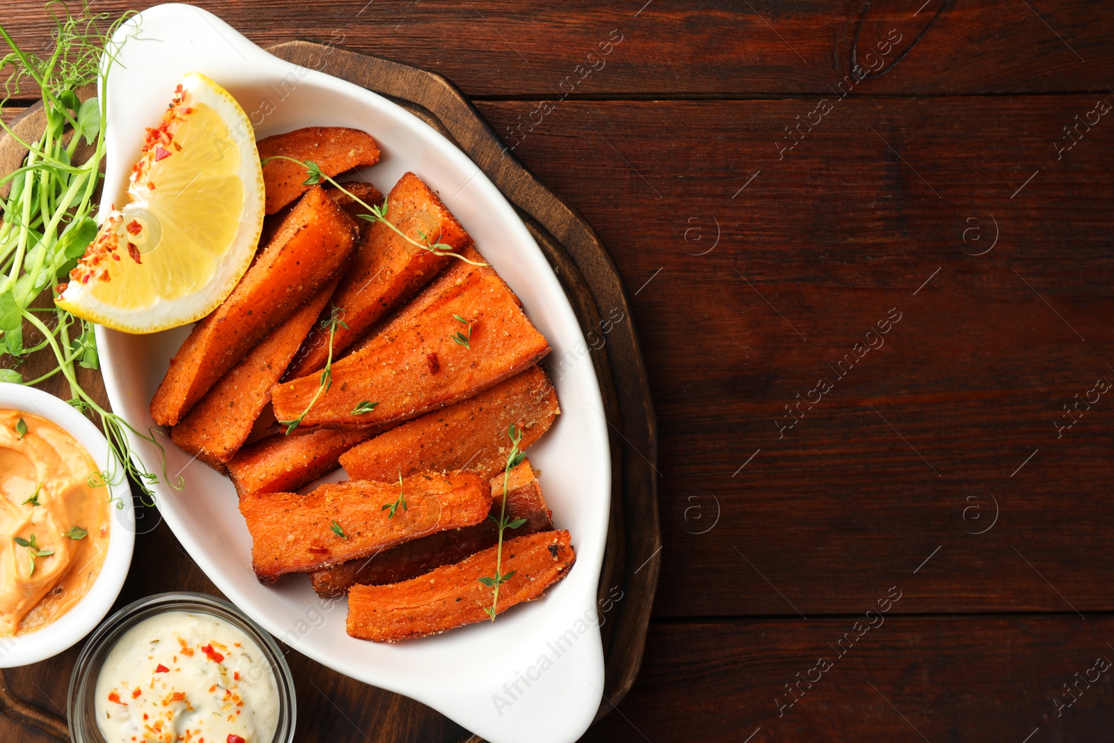 Photo of Pieces of tasty cooked sweet potato in baking dish served on wooden table, top view. Space for text