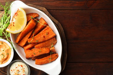 Photo of Pieces of tasty cooked sweet potato in baking dish served on wooden table, top view. Space for text