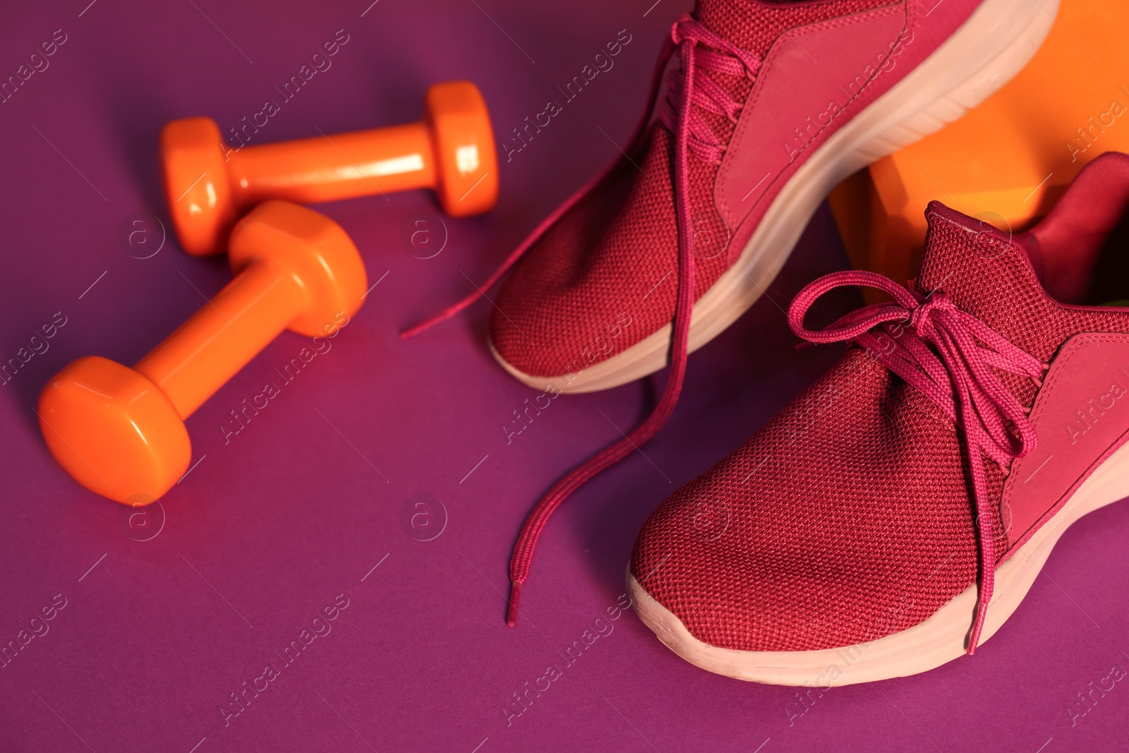 Photo of Stylish sneakers, dumbbells and yoga block on bright background, closeup