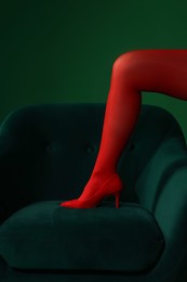 Photo of Woman in red tights and heels showing leg on green background, closeup