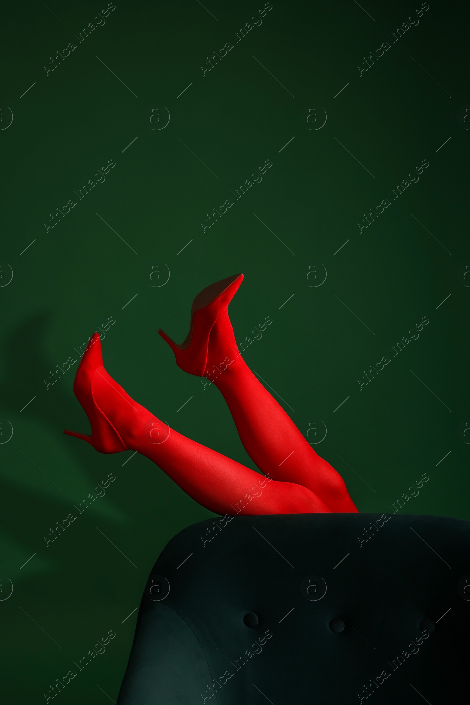 Photo of Woman in red tights and heels showing legs on green background, closeup