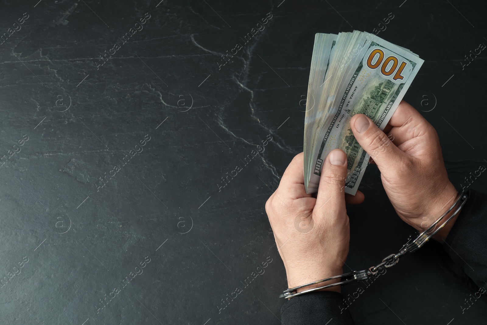 Photo of Corruption. Man in handcuffs with dollar banknotes at grey textured table, closeup. Space for text