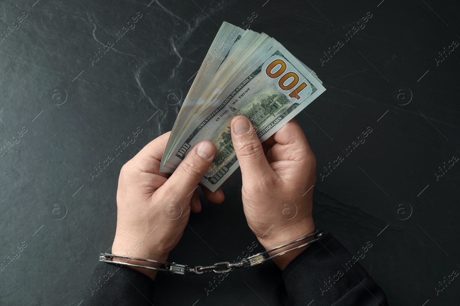 Photo of Corruption. Man in handcuffs holding dollar banknotes at grey textured table, closeup