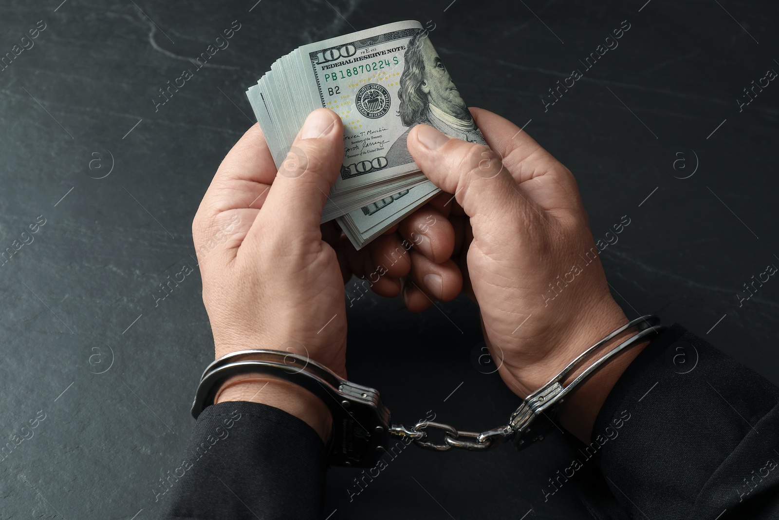 Photo of Corruption. Man in handcuffs holding dollar banknotes at grey textured table, closeup