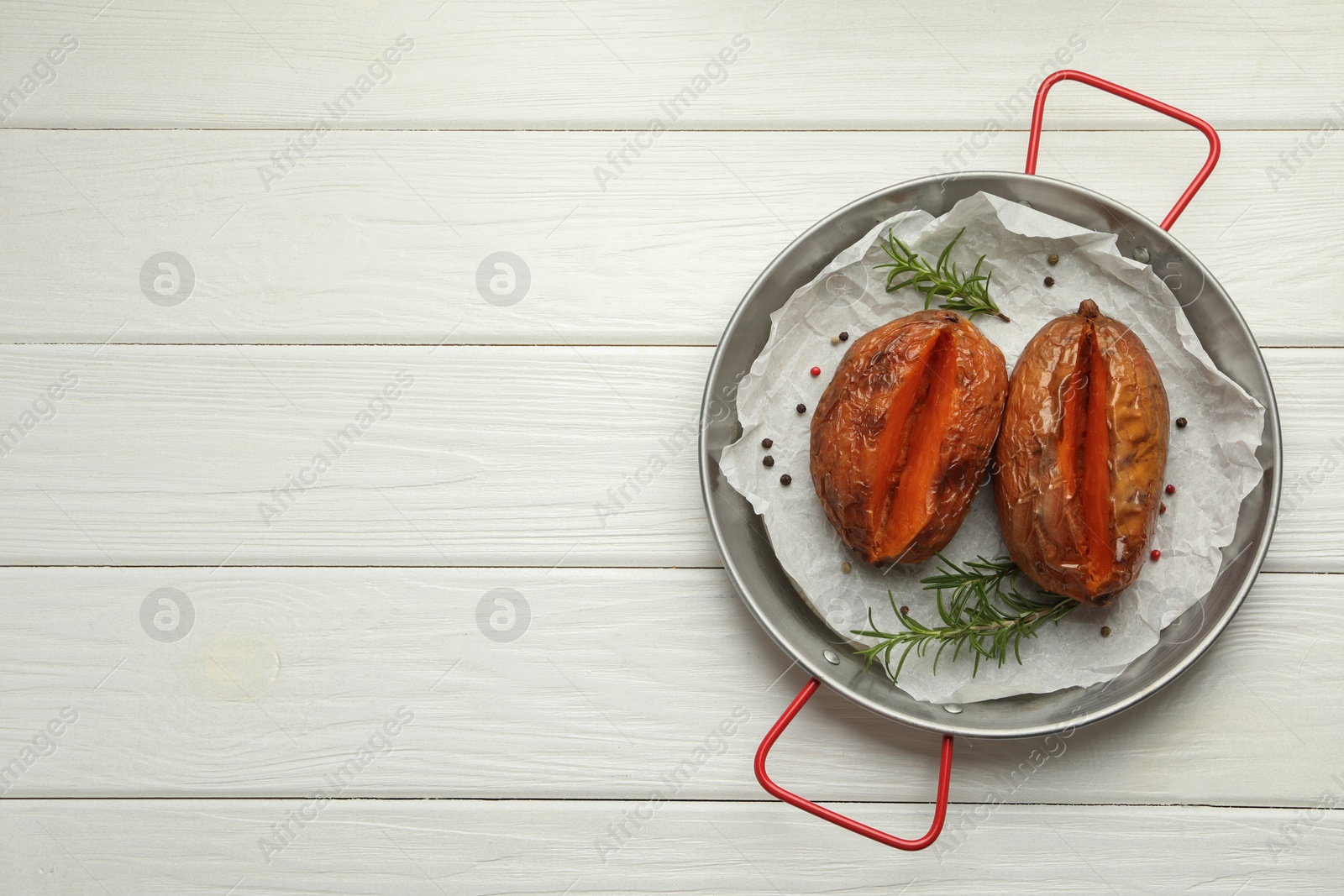 Photo of Tasty cooked sweet potatoes with rosemary on white wooden table, top view. Space for text