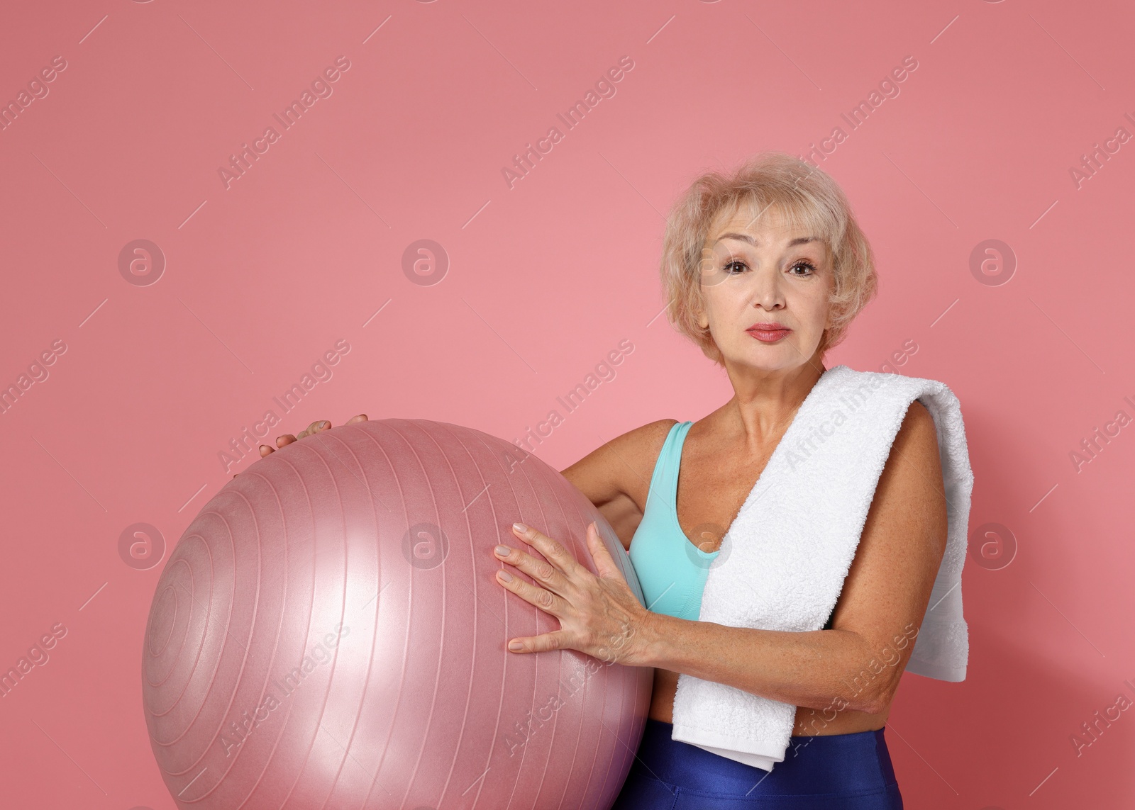 Photo of Senior woman with towel and fitness ball on pink background. Space for text