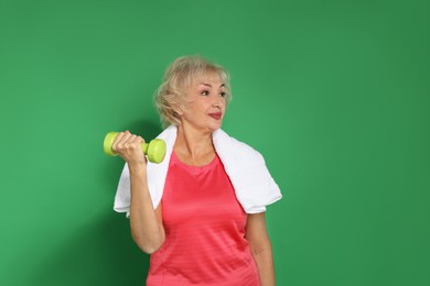 Photo of Senior woman exercising with dumbbell and towel on green background