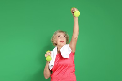 Photo of Senior woman exercising with dumbbells and towel on green background