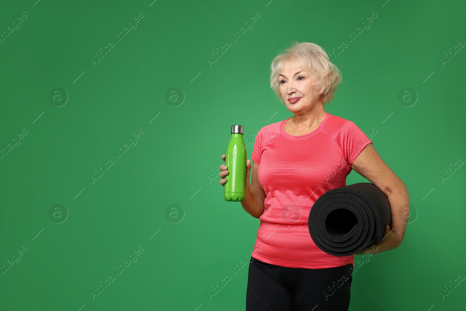 Photo of Senior woman with fitness mat and water on green background, space for text