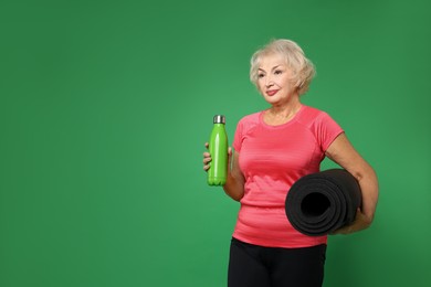 Photo of Senior woman with fitness mat and water on green background, space for text