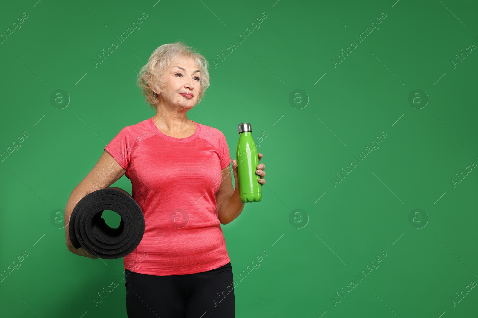 Photo of Senior woman with fitness mat and water on green background, space for text