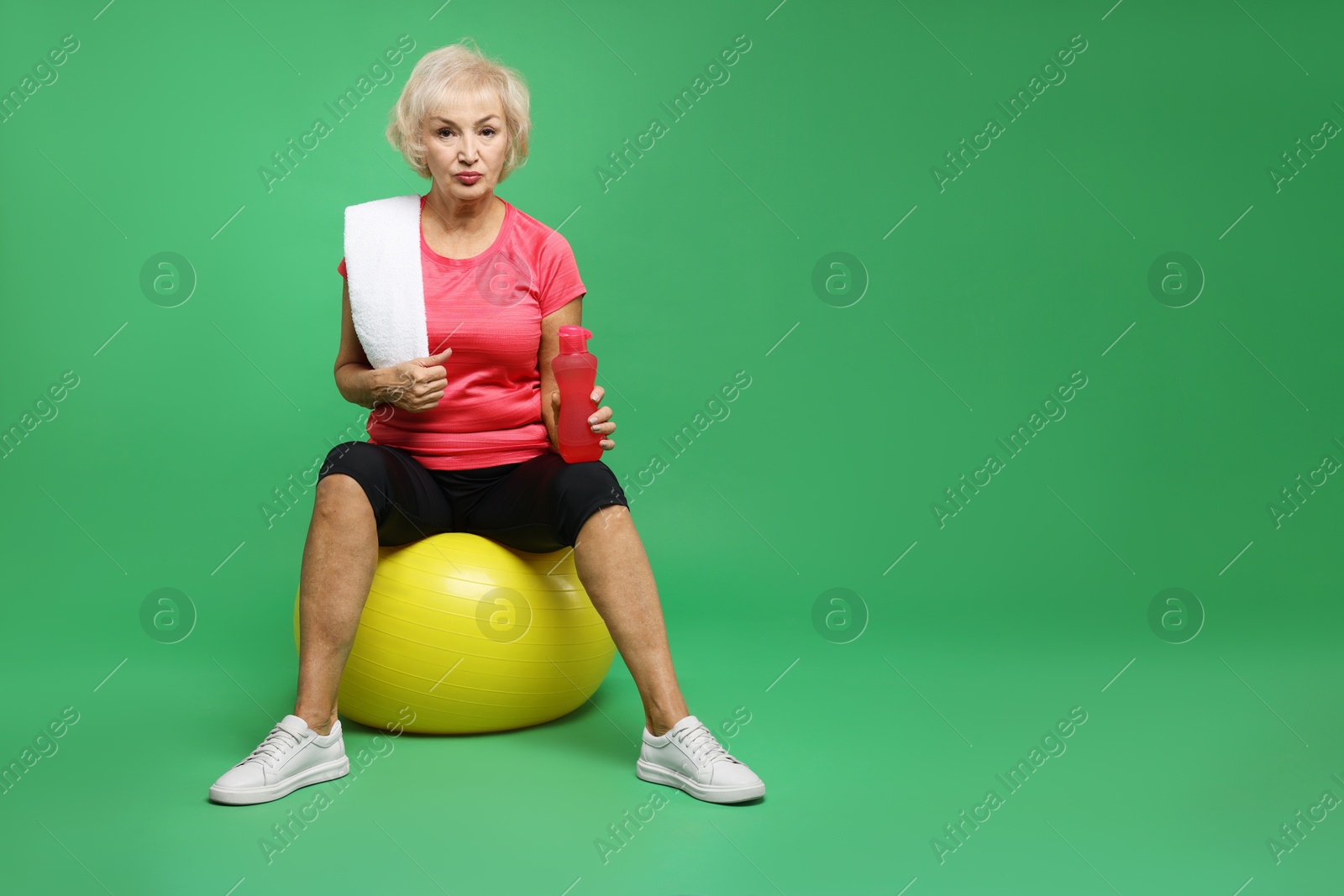 Photo of Senior woman with fitness ball, water and towel on green background, space for text