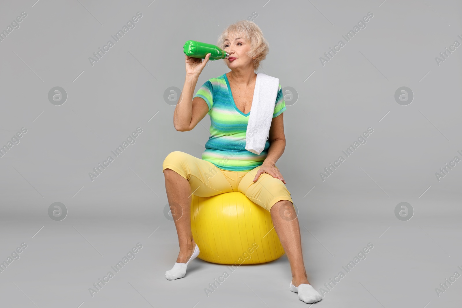 Photo of Senior woman with fitness ball, water and towel on light grey background