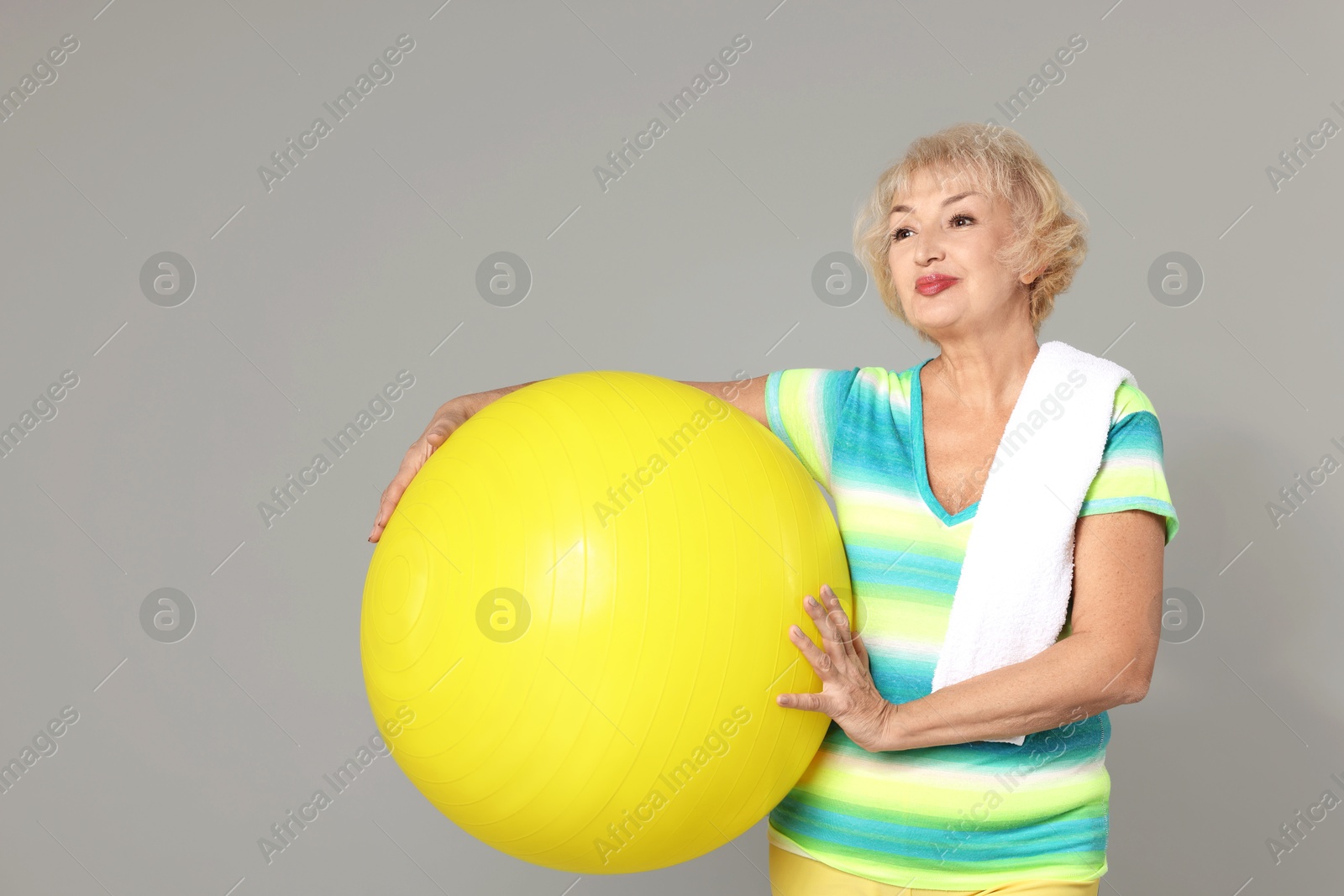 Photo of Senior woman with fitness ball and towel on light grey background