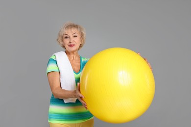 Photo of Senior woman with fitness ball and towel on light grey background