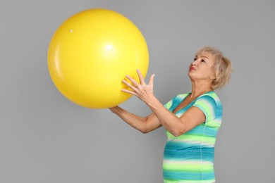 Photo of Senior woman with fitness ball on light grey background