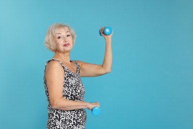 Photo of Senior woman exercising with dumbbells on light blue background, space for text