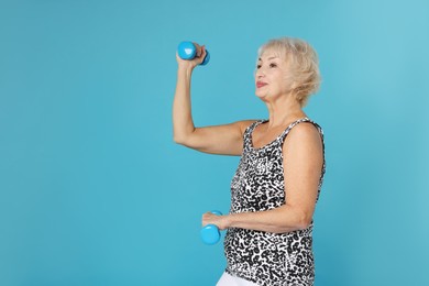 Photo of Senior woman exercising with dumbbells on light blue background, space for text