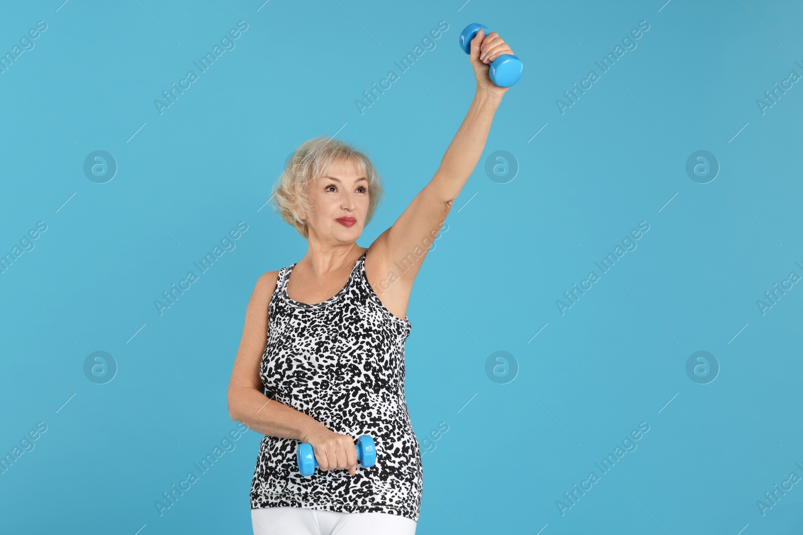 Photo of Senior woman exercising with dumbbells on light blue background, space for text