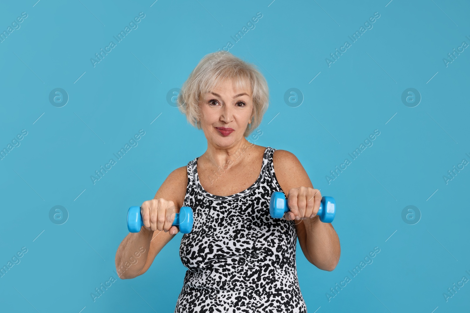 Photo of Senior woman exercising with dumbbells on light blue background