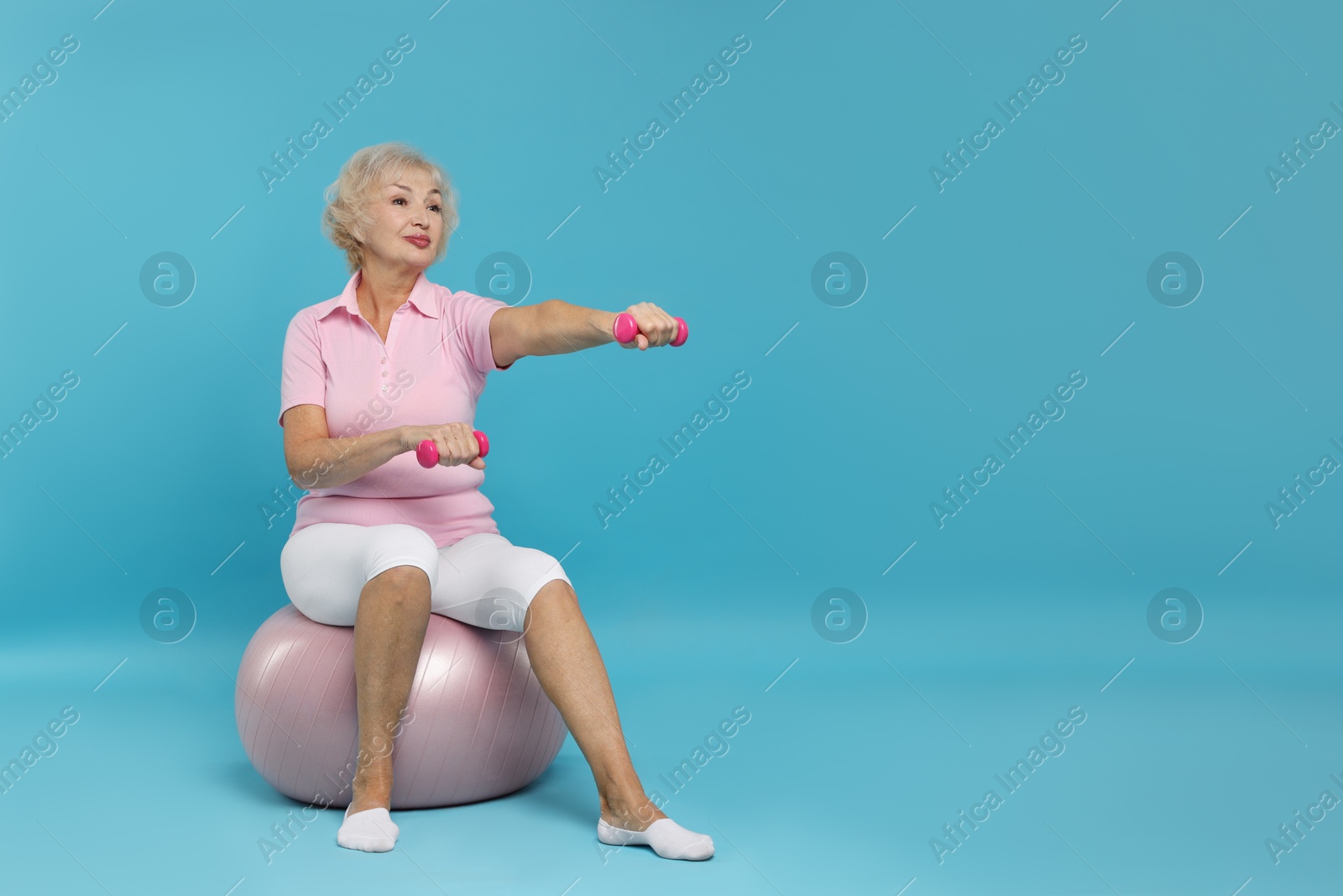 Photo of Senior woman exercising with fitness ball and dumbbells on light blue background, space for text