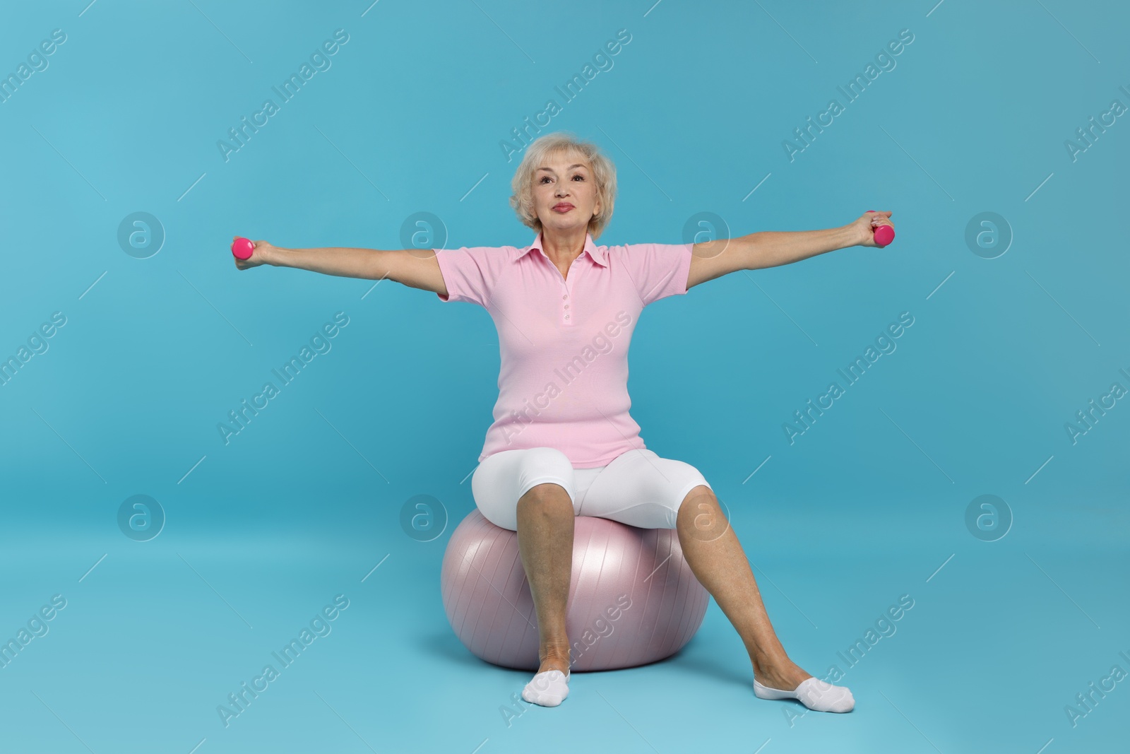 Photo of Senior woman exercising with fitness ball and dumbbells on light blue background