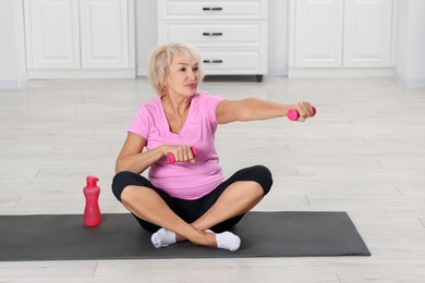 Photo of Senior woman exercising with fitness mat and dumbbells at home