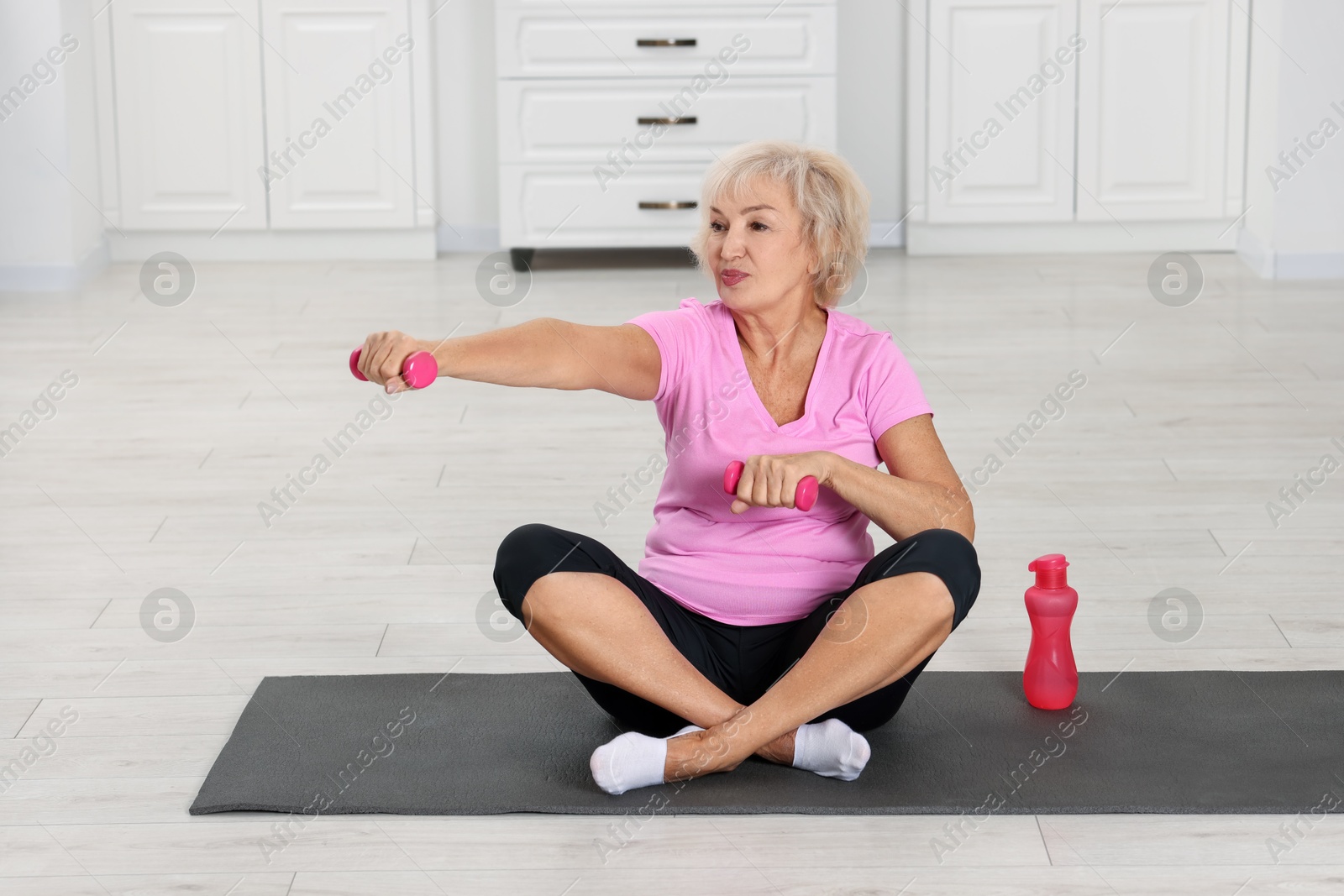 Photo of Senior woman exercising with fitness mat and dumbbells at home