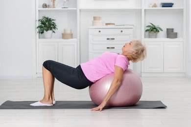 Photo of Senior woman exercising with fitness mat and ball at home