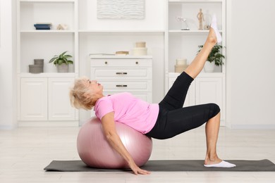 Photo of Senior woman exercising with fitness mat and ball at home