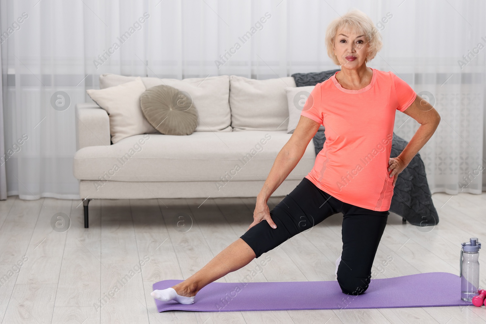 Photo of Senior woman exercising with fitness mat at home, space for text