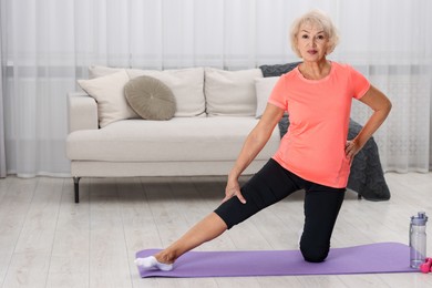 Photo of Senior woman exercising with fitness mat at home, space for text