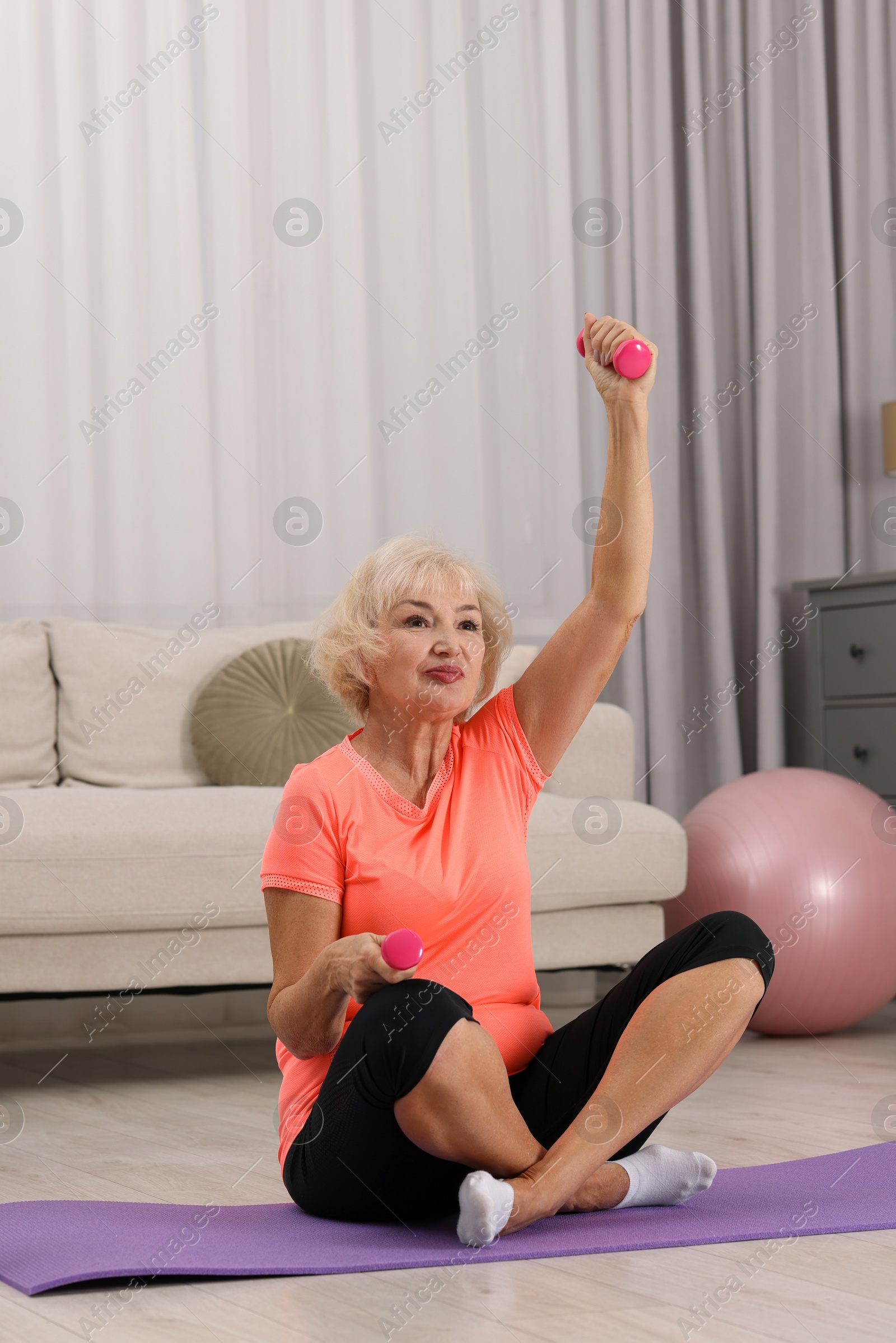 Photo of Senior woman exercising with fitness mat and dumbbells at home