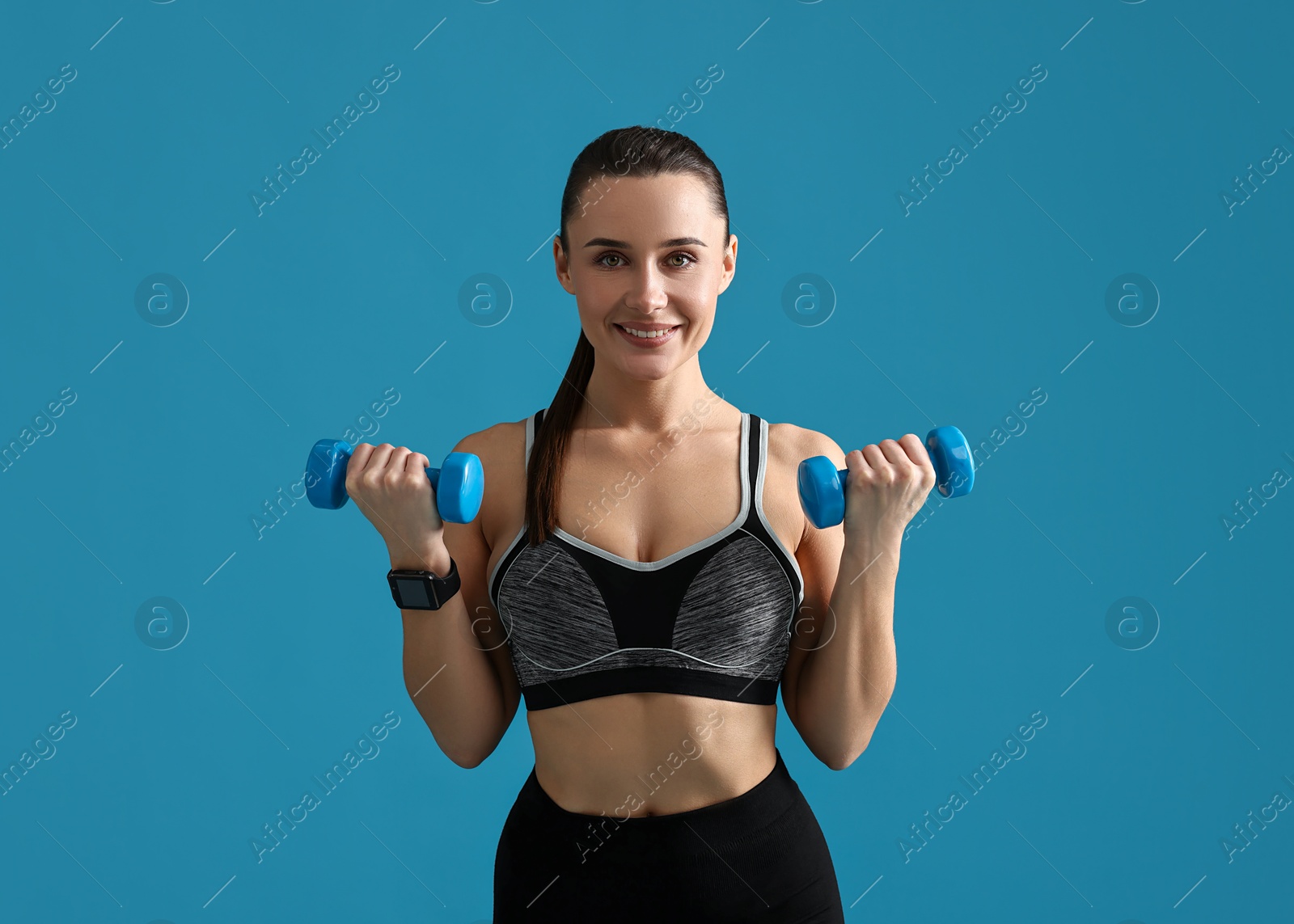 Photo of Woman in gym clothes exercising with dumbbells on light blue background