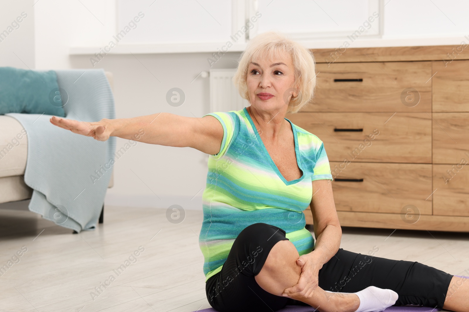 Photo of Senior woman exercising with fitness mat at home