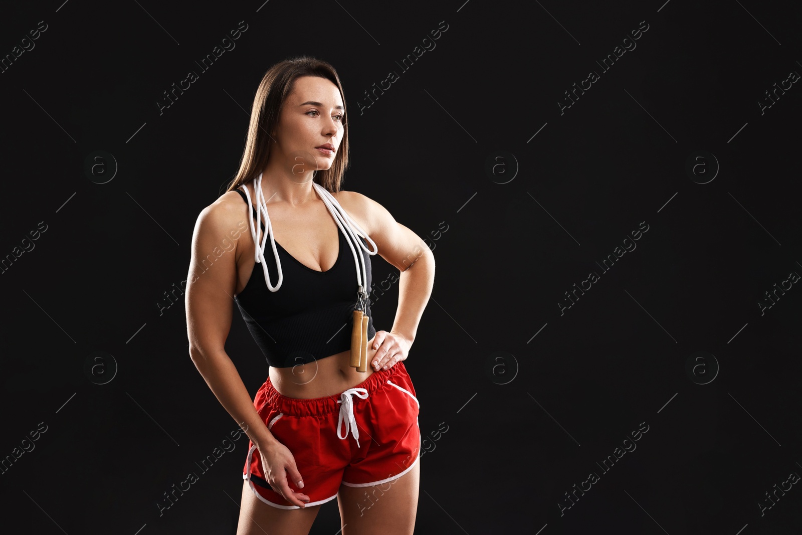 Photo of Woman in gym clothes with skipping rope on black background, space for text