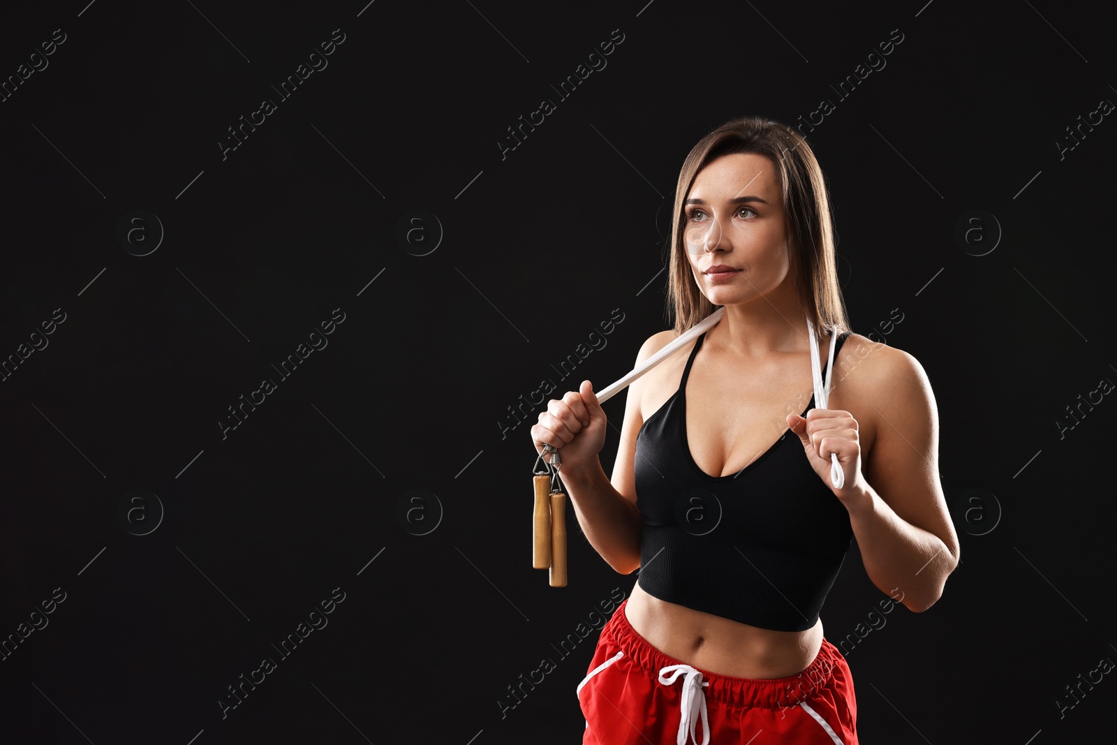 Photo of Woman in gym clothes with skipping rope on black background, space for text