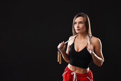 Photo of Woman in gym clothes with skipping rope on black background, space for text