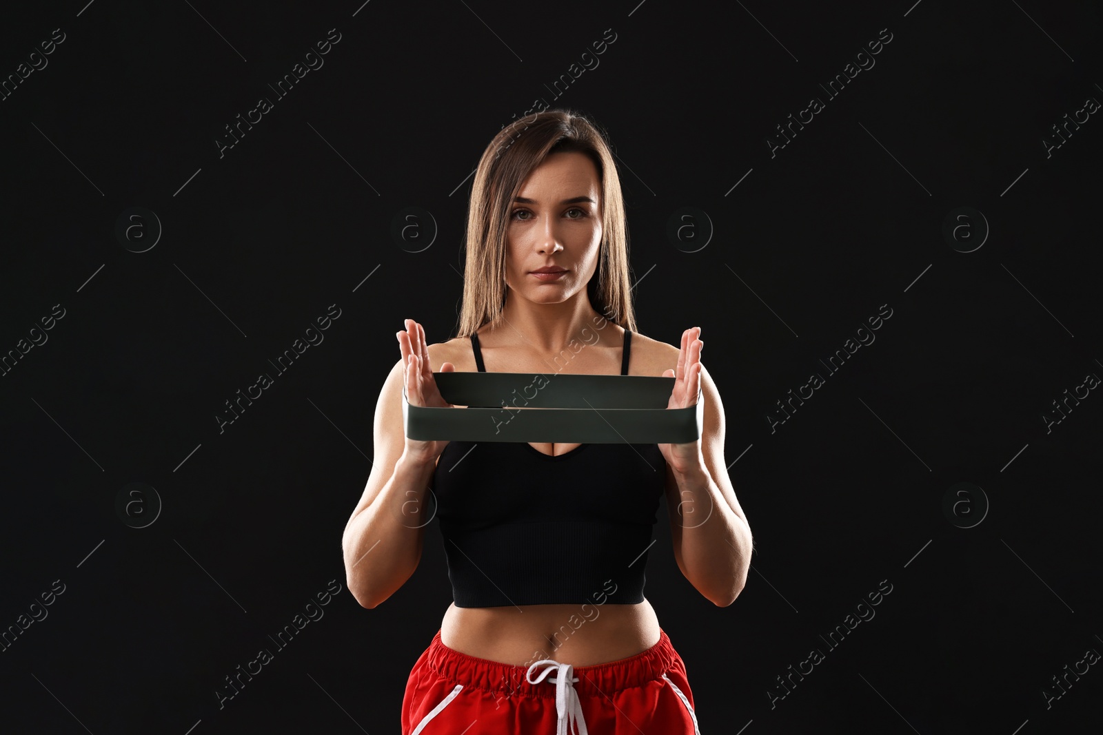 Photo of Woman in gym clothes with elastic band on black background