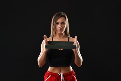 Photo of Woman in gym clothes with elastic band on black background