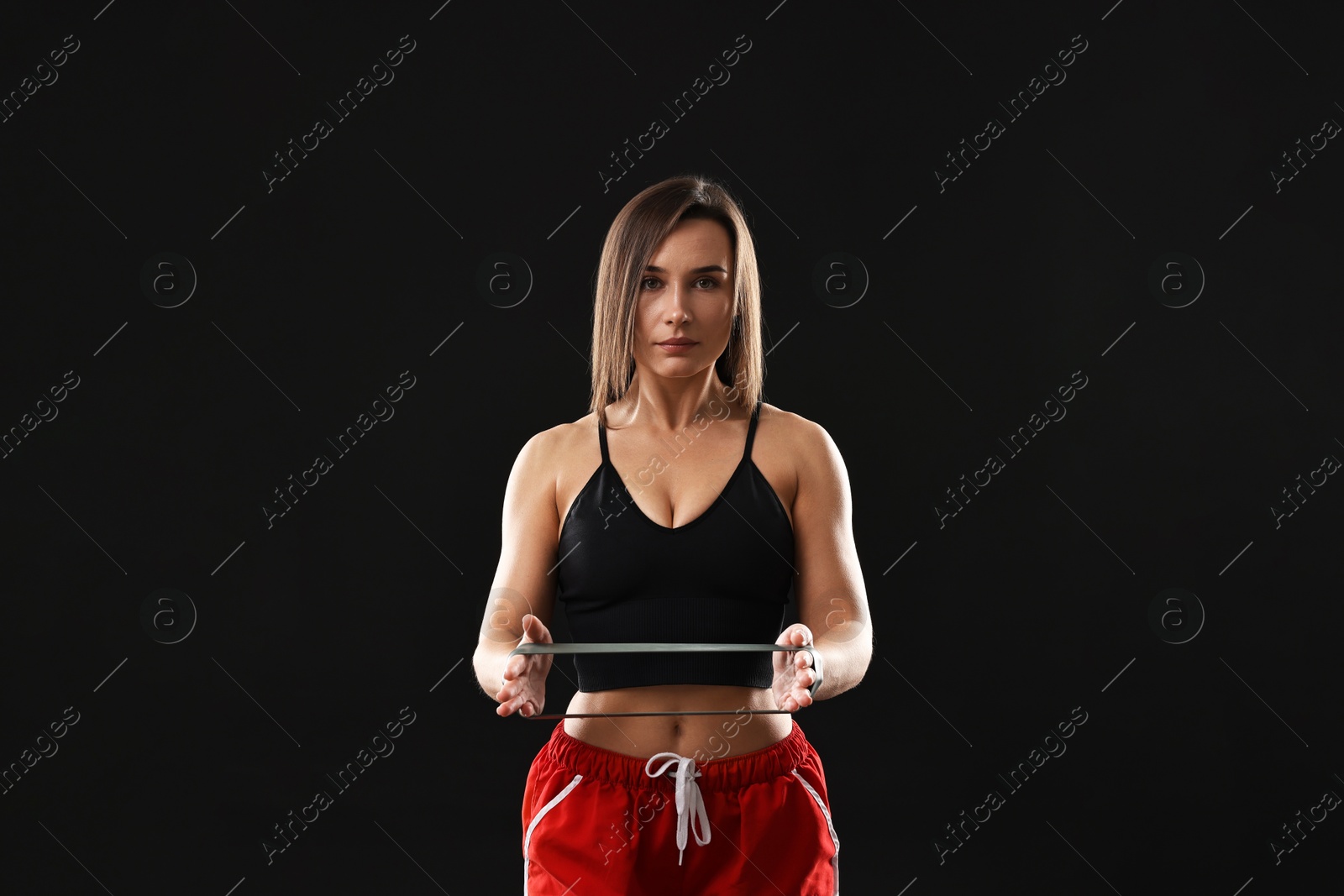 Photo of Woman in gym clothes with elastic band on black background