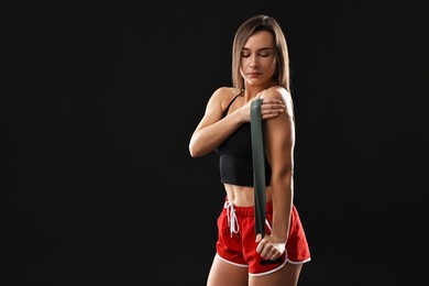 Photo of Woman in gym clothes doing exercise with elastic band on black background, space for text