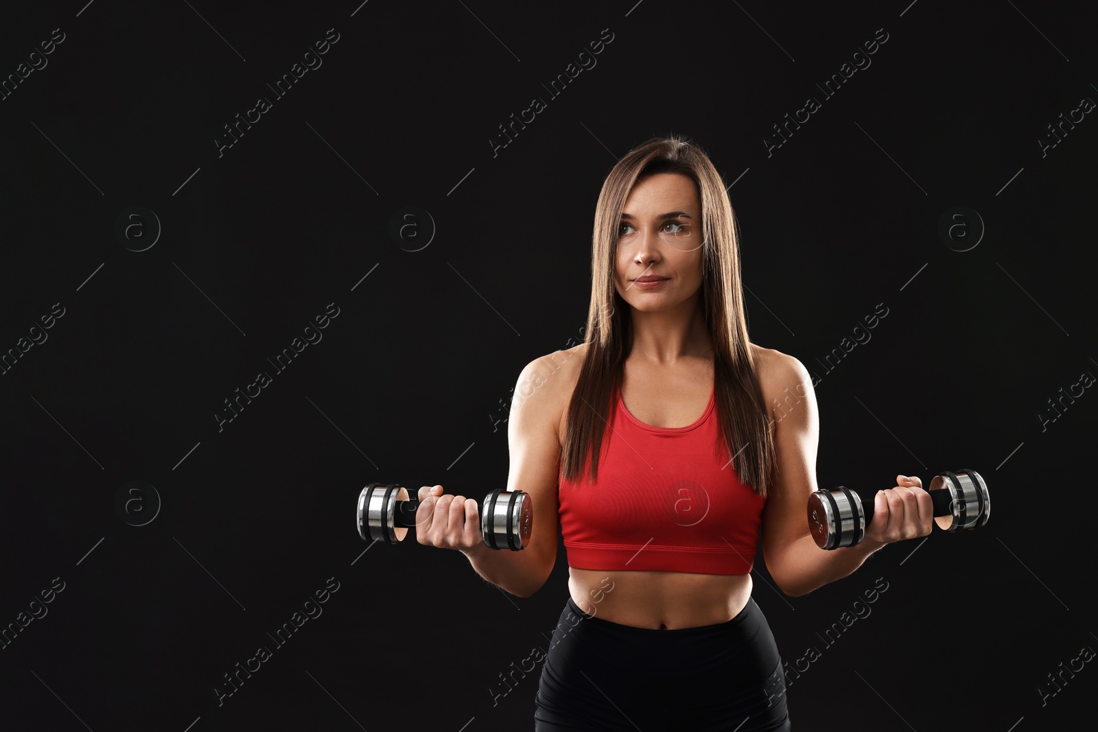 Photo of Woman in gym clothes exercising with dumbbells on black background, space for text