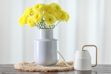 Photo of Beautiful yellow flowers in vase and watering can on wooden table at home