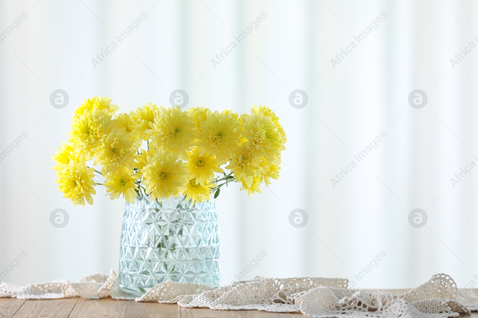 Photo of Beautiful yellow flowers in vase on wooden table at home. Space for text