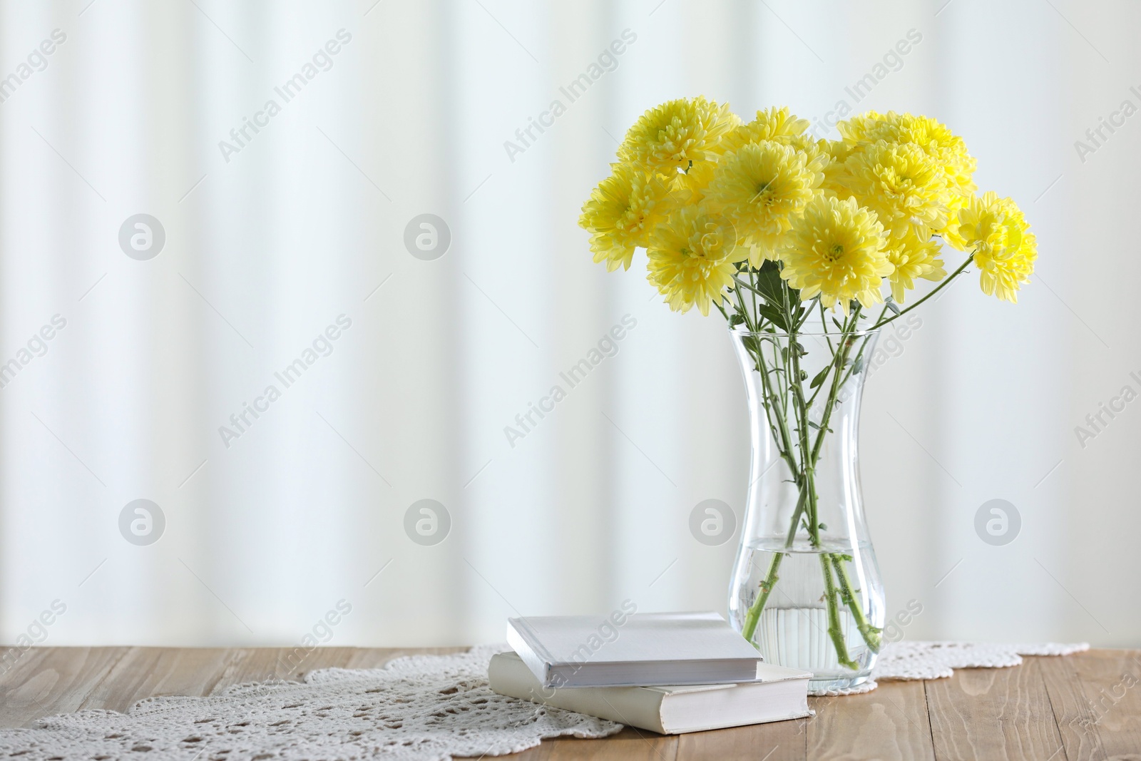 Beautiful yellow flowers in vase and books on wooden table at home. Space for text Photo of Beautiful yellow flowers in vase and books on wooden table at home. Space for text