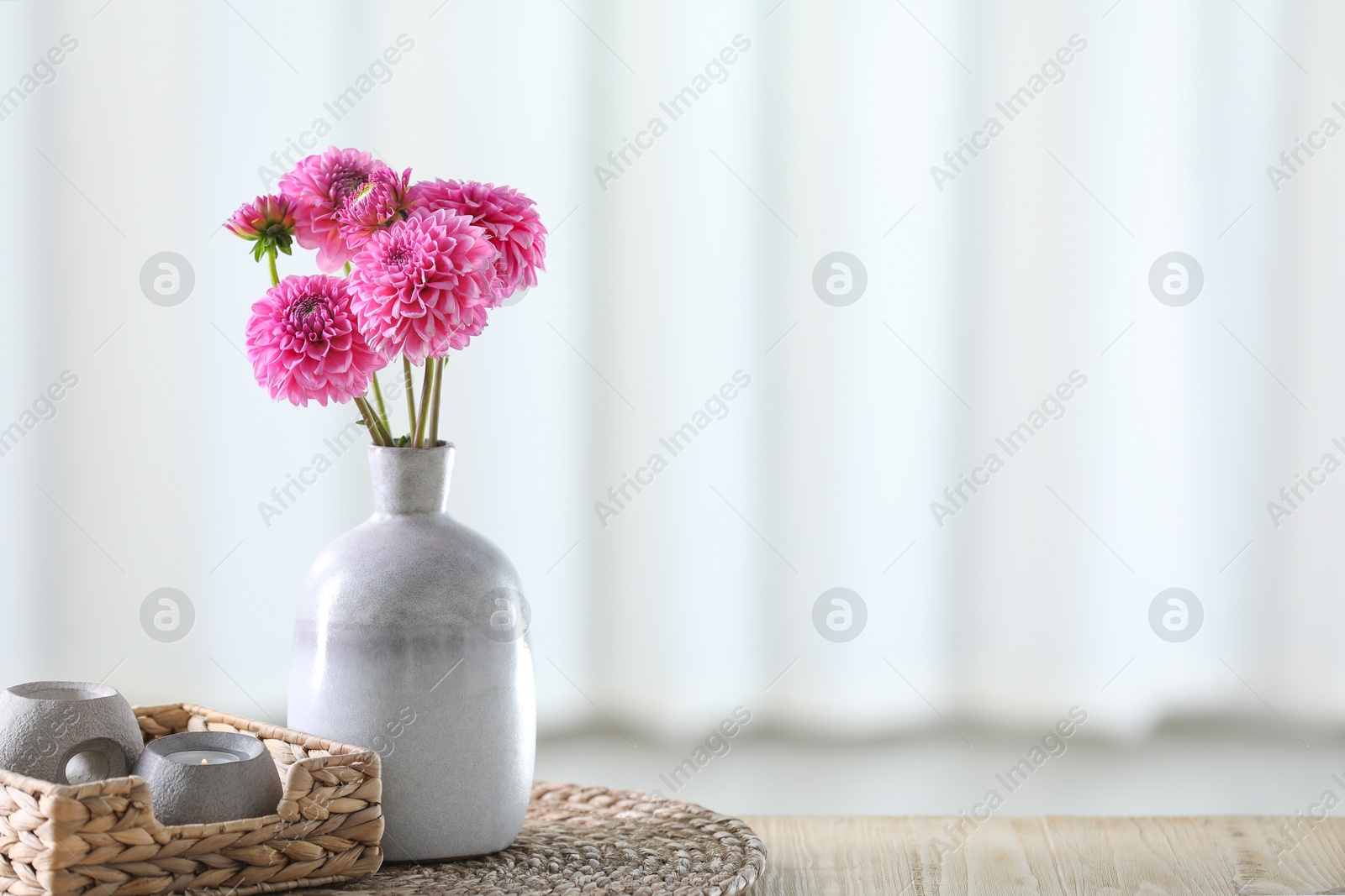 Photo of Beautiful pink flowers in vase and burning candle on wooden table at home. Space for text